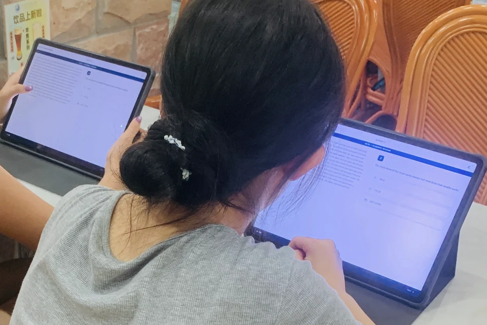 从成年学习者肩后拍摄的平板 IELTS 阅读练习